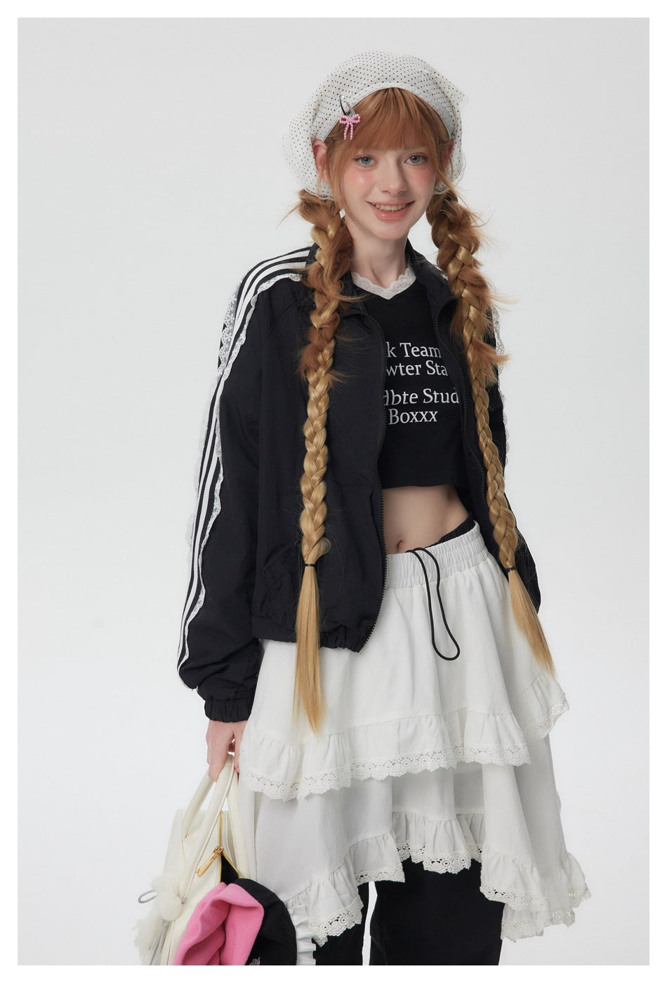 Front view of a model in a black zip jacket with white lace-trim stripes, a black top, and a white tiered skirt.