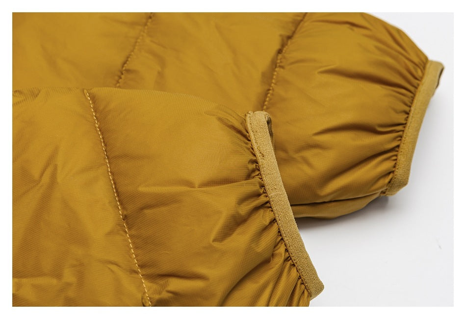 Close-up of a mustard-gold padded jacket showing stitched panels and a narrow tan fabric tab along a gathered edge.