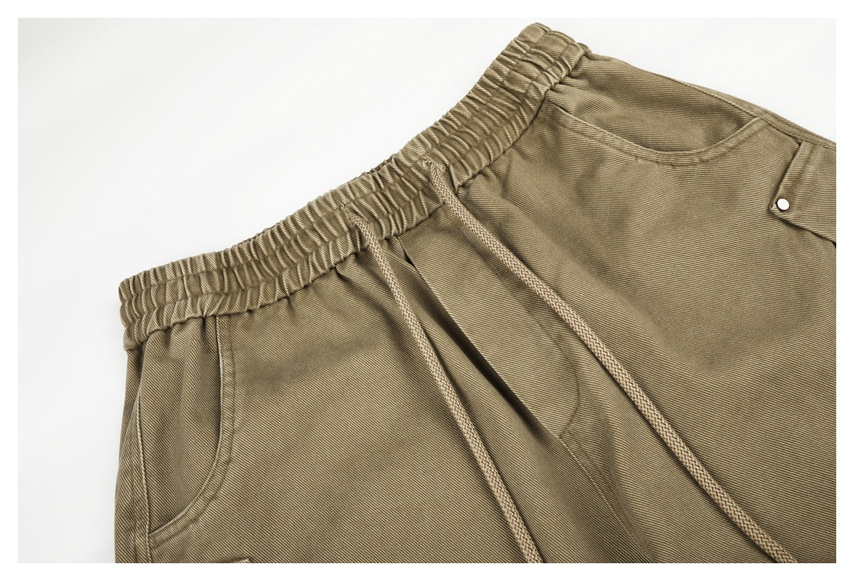 Close-up of khaki trousers showing an elastic waistband, drawstrings, curved pocket, and a small flap pocket with a snap.