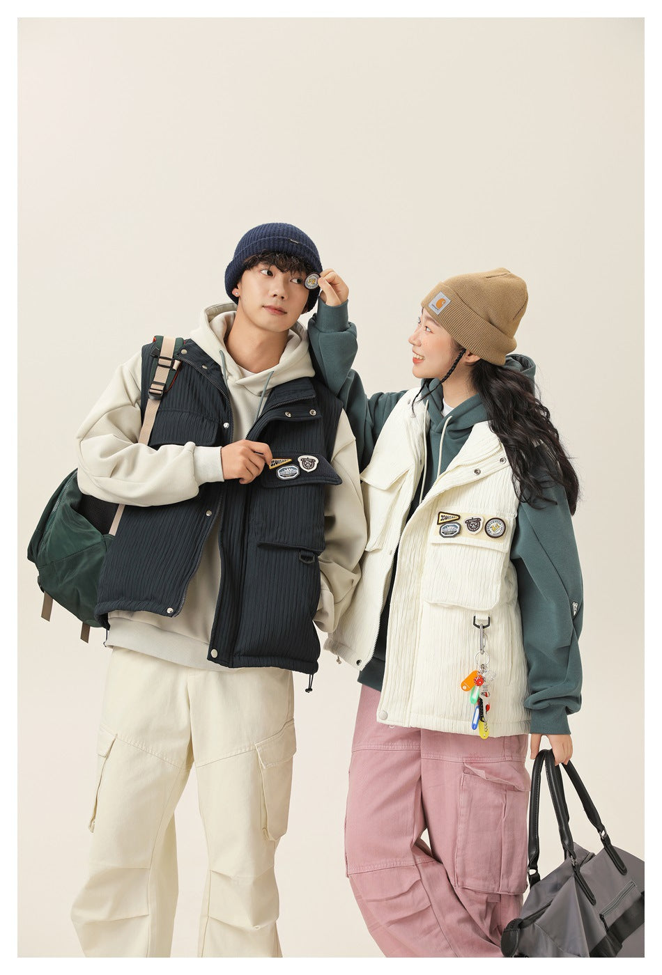 Two models in cream and navy utility vests over hoodies, with the cream vest shown prominently.