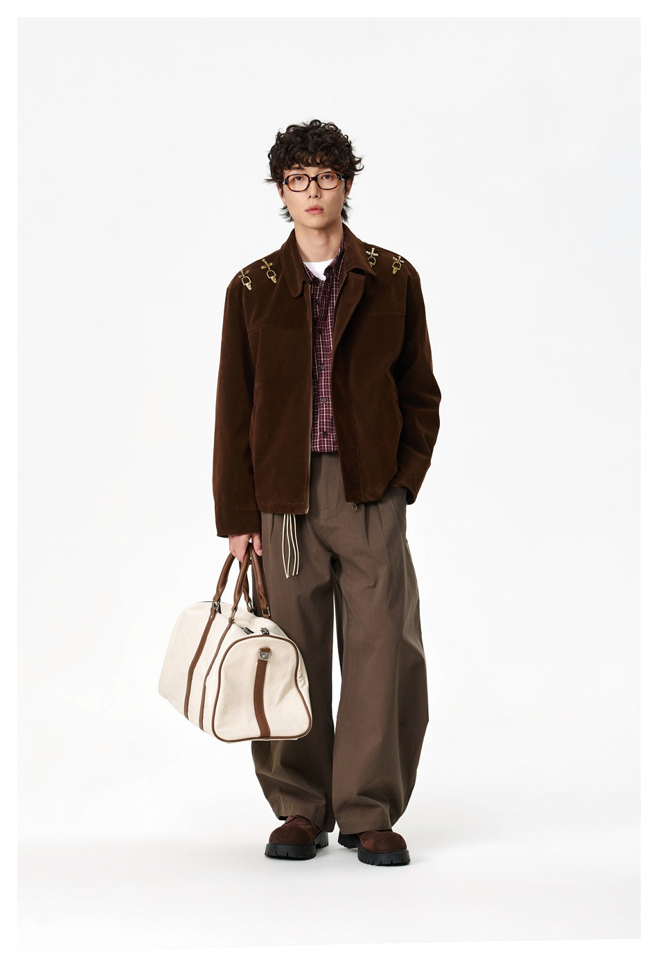 Full-length view of a model wearing a dark brown jacket with brass shoulder hardware and loose brown trousers.