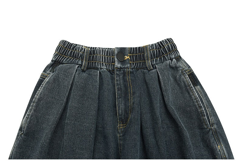 Front waist and upper legs of dark denim pants, showing an elastic waistband, button, and pleats.