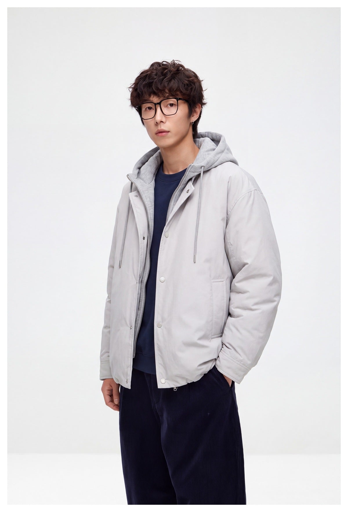 Man in glasses wearing a gray hooded jacket with the front open over a navy sweatshirt, hand in pocket