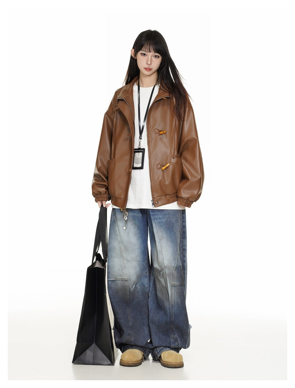 Model wearing a brown oversized jacket with toggle closures, a white shirt, and loose two-tone blue jeans.