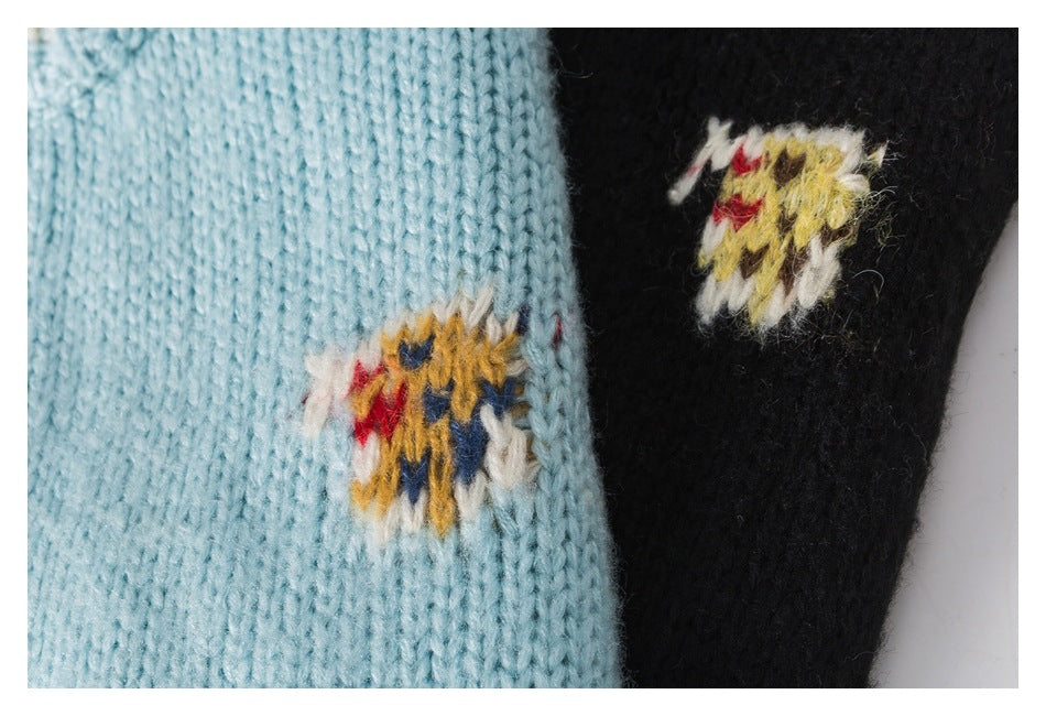 Close-up of aqua and black knit fabric with small multicolor embroidered motifs.