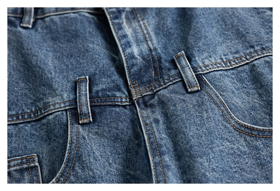 Close-up of blue washed jeans showing the fly stitching, belt loops and curved front pocket edges.