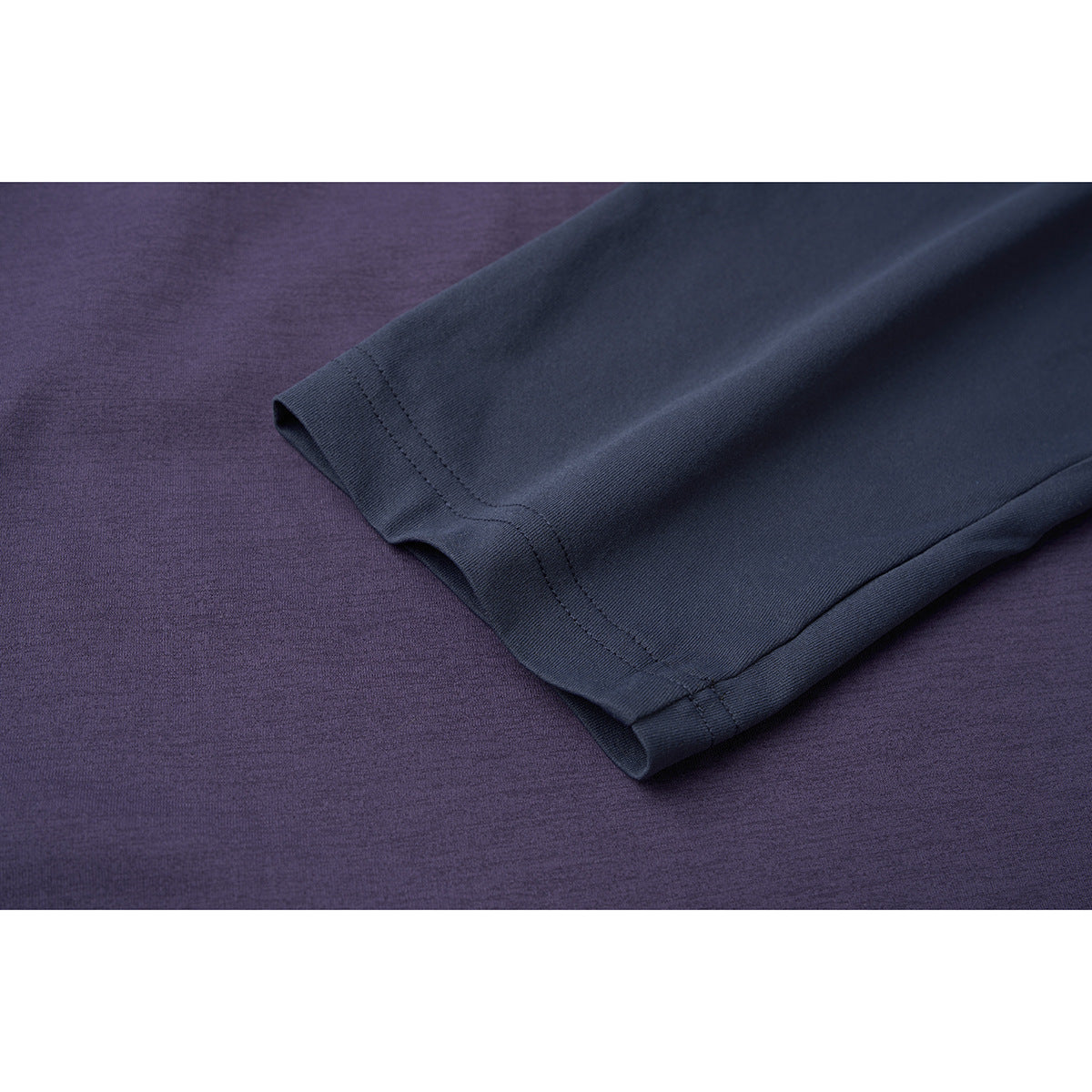 Close-up of a dark navy sleeve cuff and stitched hem against the purple body of a top.