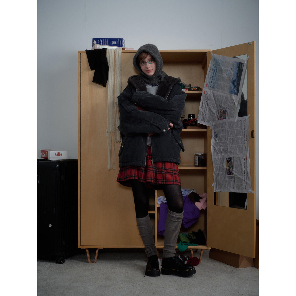 Full-length front view of a person wearing a charcoal hooded jacket, red plaid skirt, black tights and gray leg warmers.