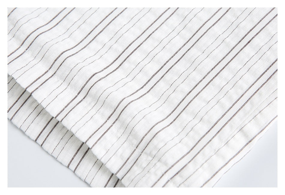 Close-up of white fabric with fine dark vertical stripes and a stitched folded edge.