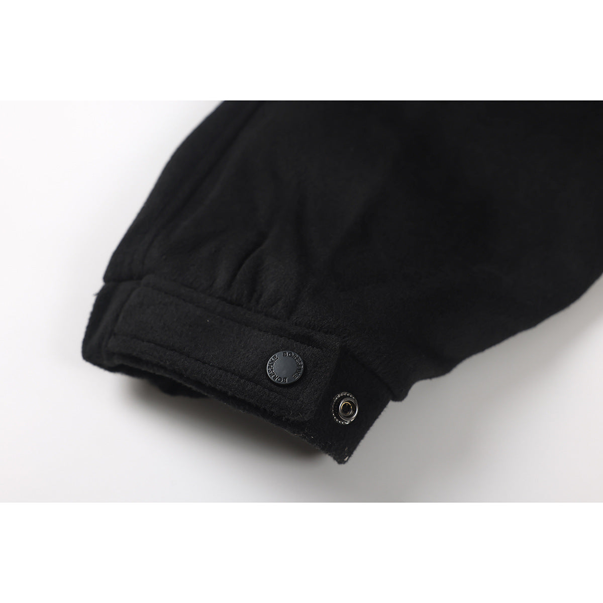 Close-up of a black jacket sleeve cuff with a snap fastener and a round button.