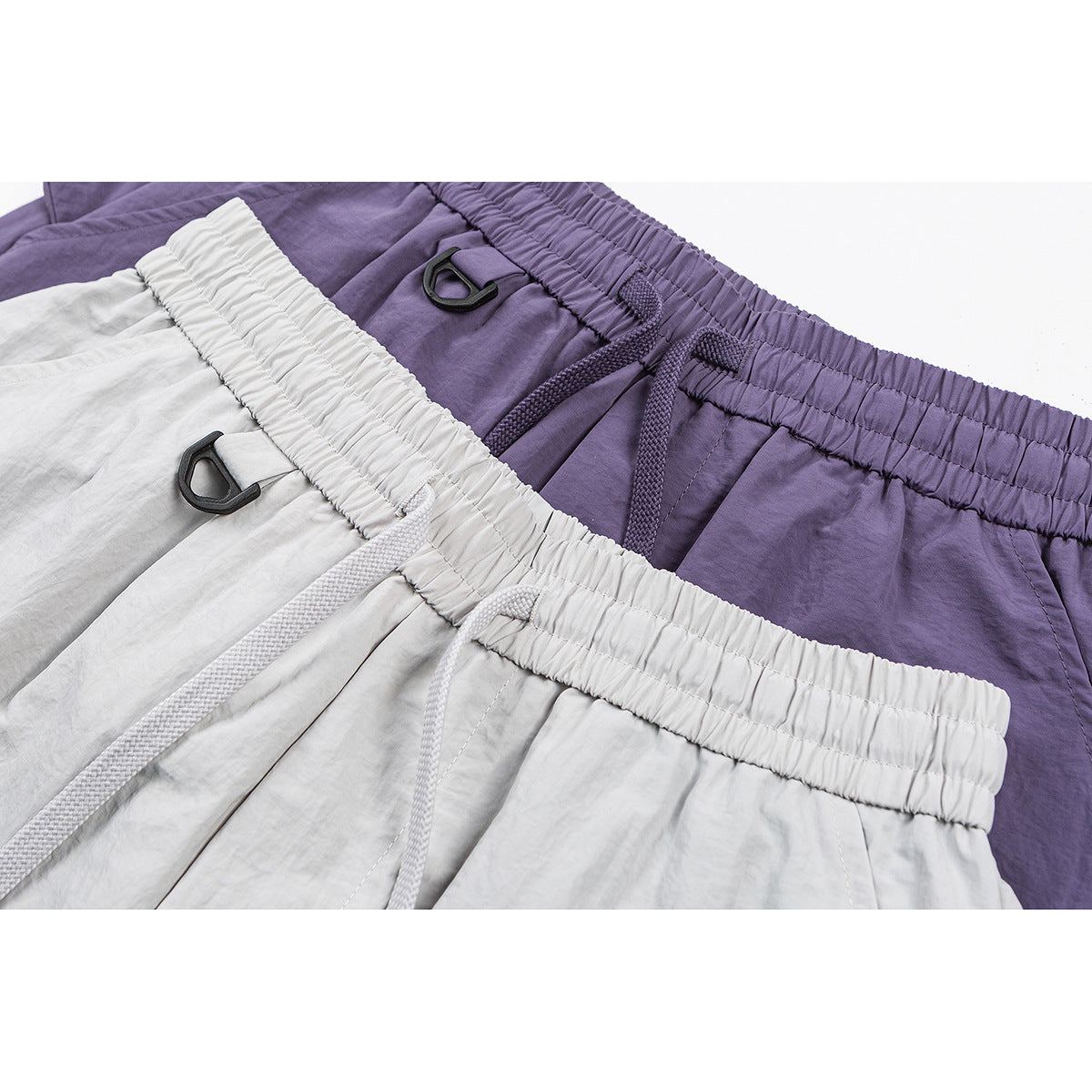 Close-up of white and purple pants showing elastic drawstring waistbands and black D-ring accents.