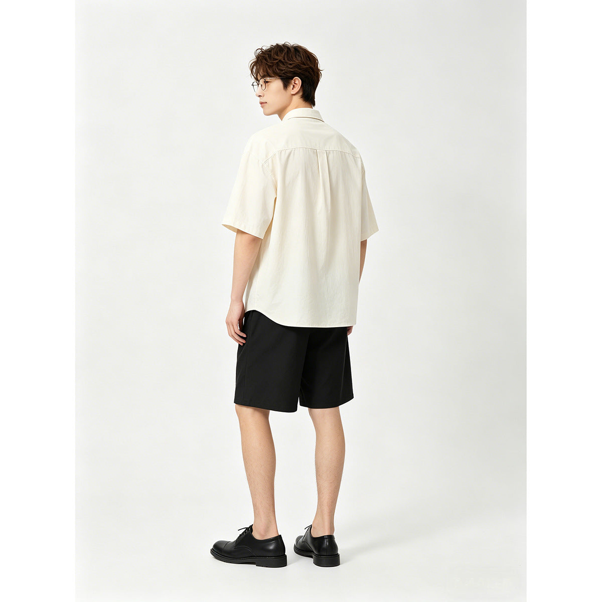 Model wearing an ivory short-sleeve shirt and black shorts, shown from the back.