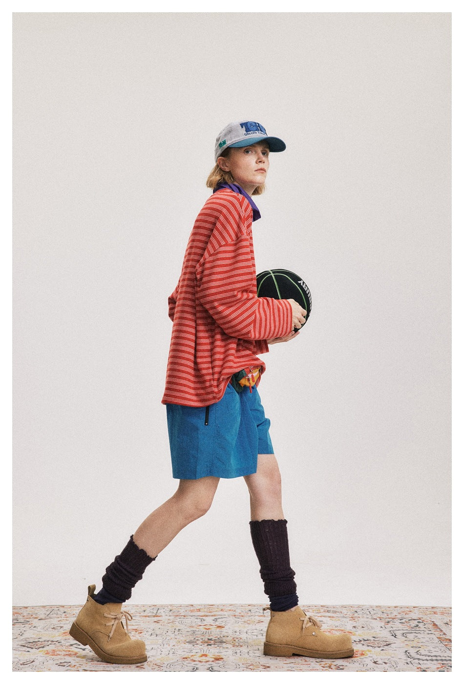 Model in a red-and-white striped long-sleeve shirt and blue shorts, holding a basketball.
