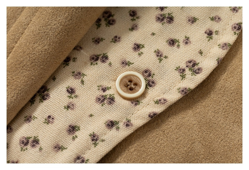 Close-up of a cream fabric strip with tiny purple flowers and a beige button against tan garment fabric.