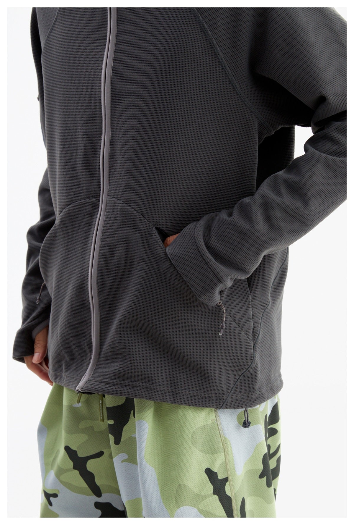 Close view of the charcoal jacket's curved zip hand pocket and hem above green camouflage pants.