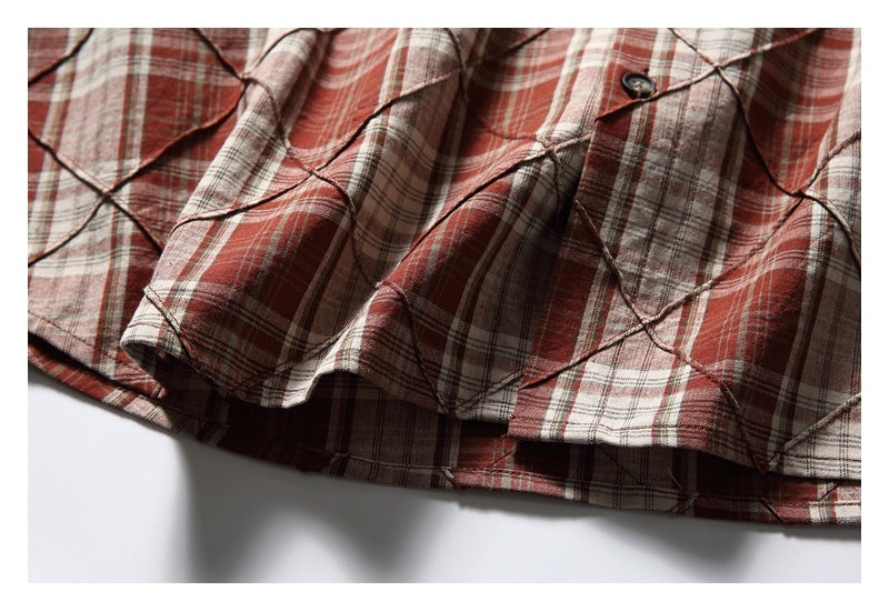 Close-up of the shirt’s curved hem and layered red, cream, and gray plaid panels.