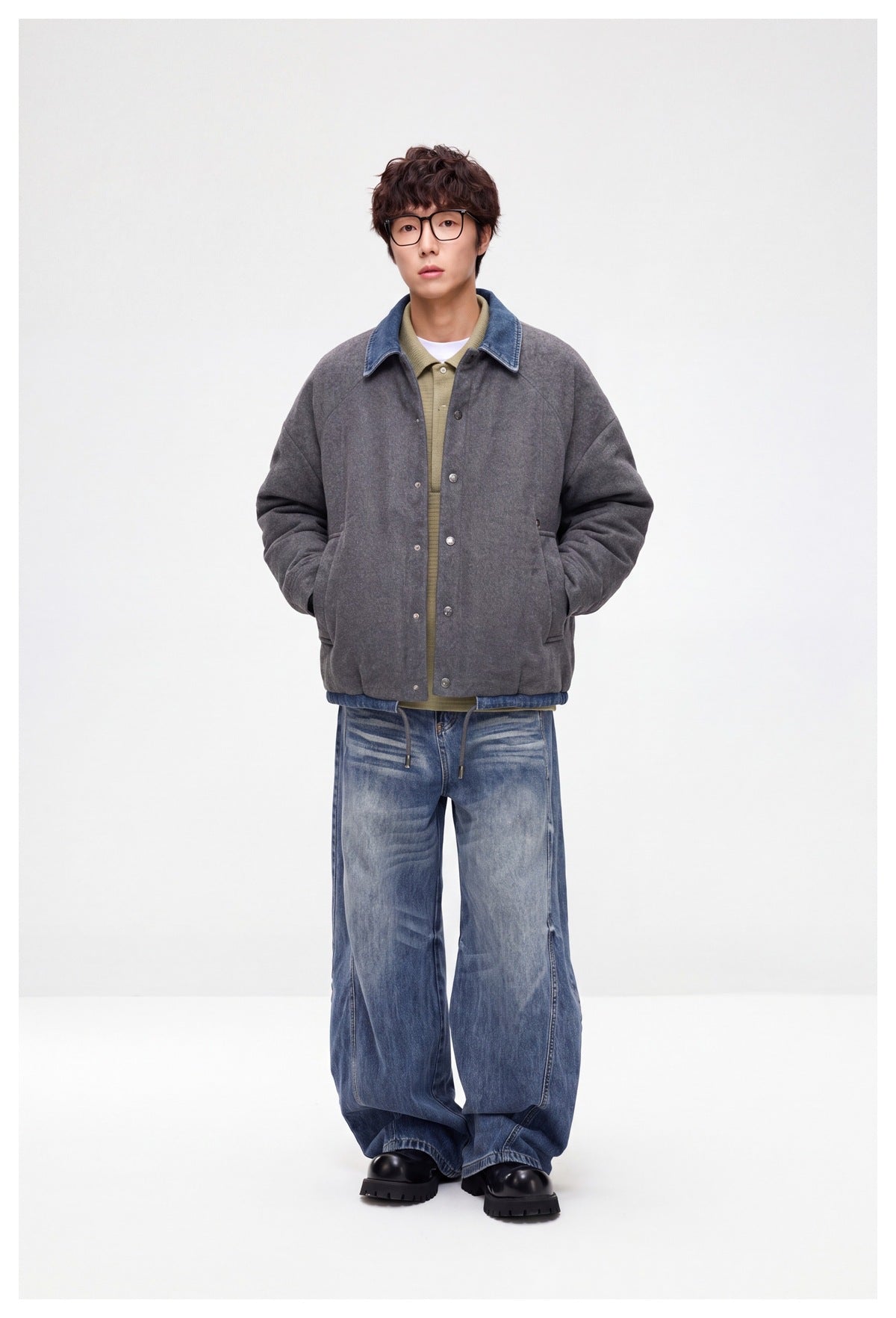 Model wearing a charcoal-gray snap-front jacket with a blue denim collar, shown with loose faded jeans.