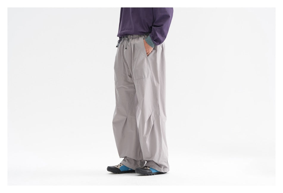 Side view of a model wearing loose light-gray trousers with a drawstring waist and blue-accented shoes.