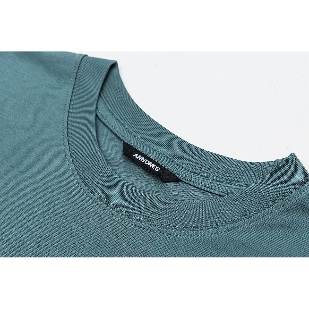 Close-up of a teal T-shirt's ribbed crew neckline, stitching, and black inner neck label.