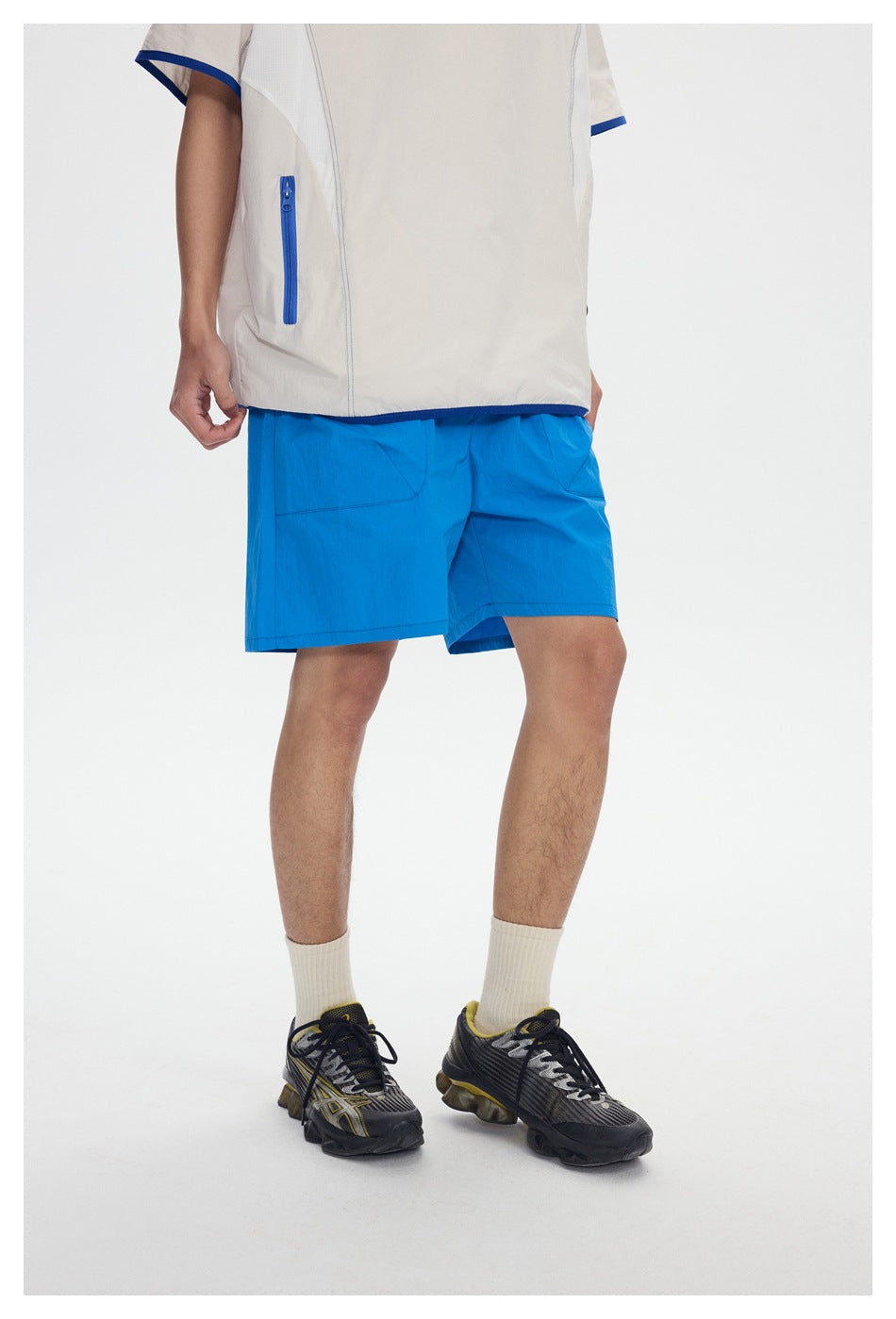 Cropped view of a model wearing bright blue shorts and an off-white top with blue trim and a zip pocket.
