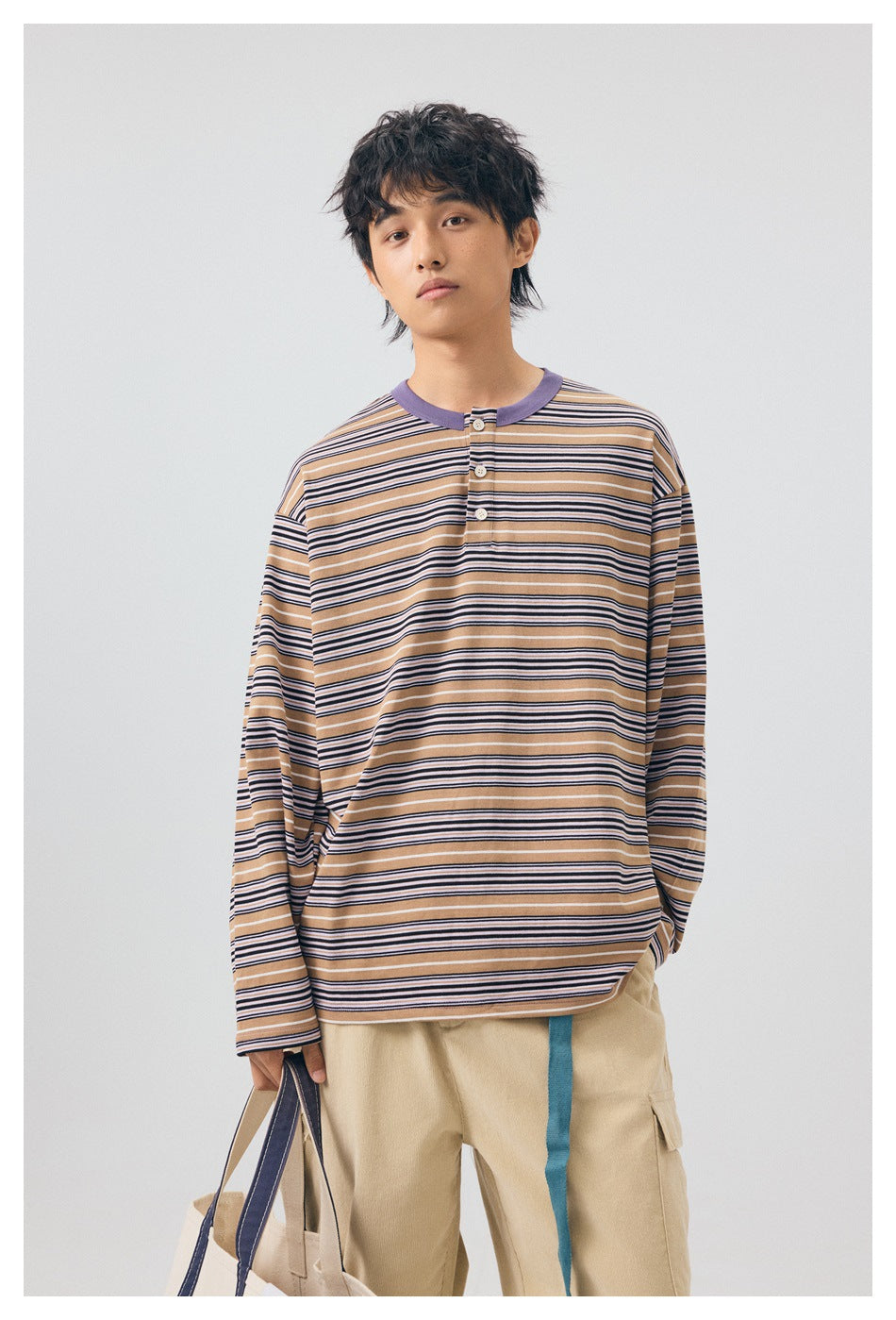Front view of a model wearing a tan, navy and white striped long-sleeve henley with a lavender collar.