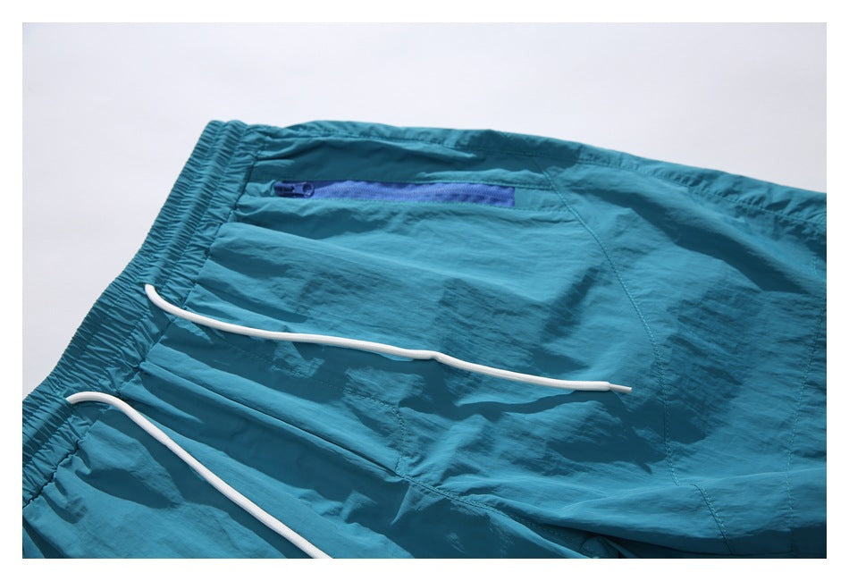 Partial flat lay of teal shorts showing white drawcords and a blue zippered pocket.