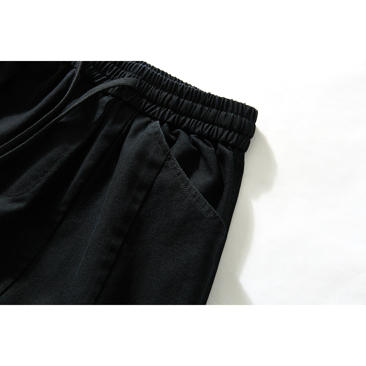 Close-up of black pants showing the gathered elastic waistband and a slanted side pocket opening.