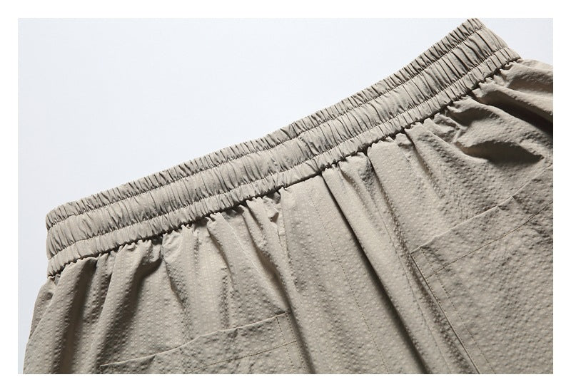 Close-up of taupe shorts showing the elastic waistband, front drawstring and top of a pocket.