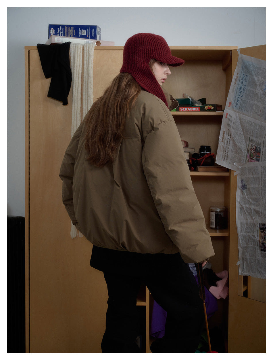 Side and back view of a model wearing a roomy taupe padded jacket with a burgundy knit hat and scarf.