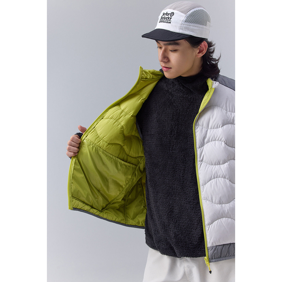 Close-up of a model opening a white quilted vest to show its bright lime-green lining.