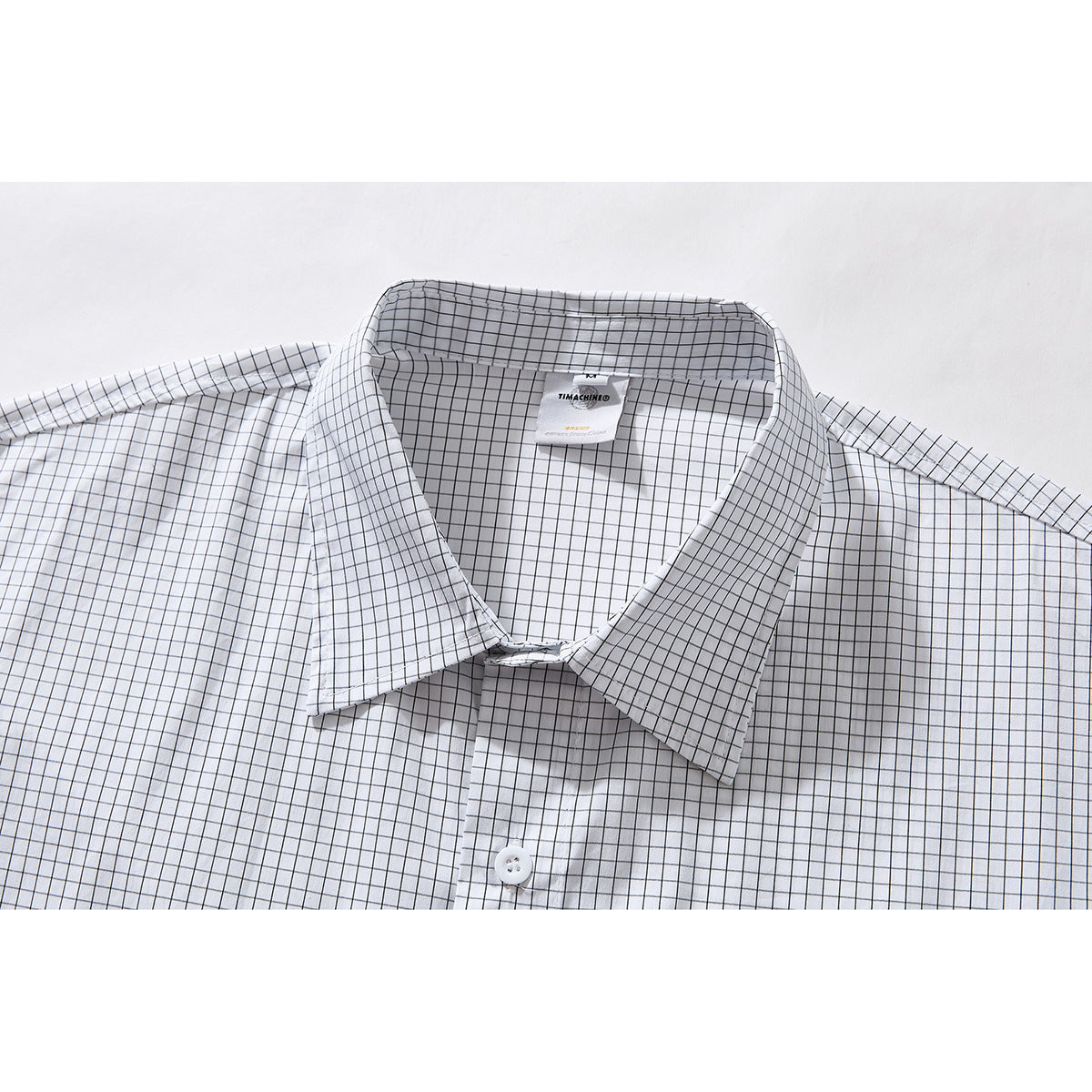 Close-up of a white button-up shirt with a fine black windowpane check, pointed collar, and visible neck label.