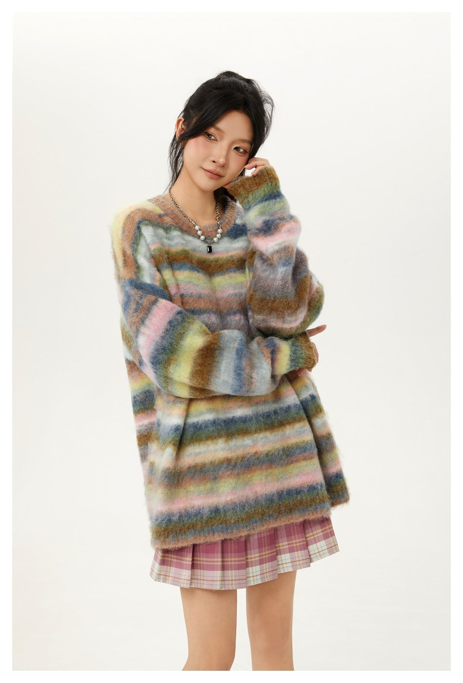 Model wearing an oversized fuzzy sweater with multicolored horizontal stripes and a pink plaid pleated skirt.