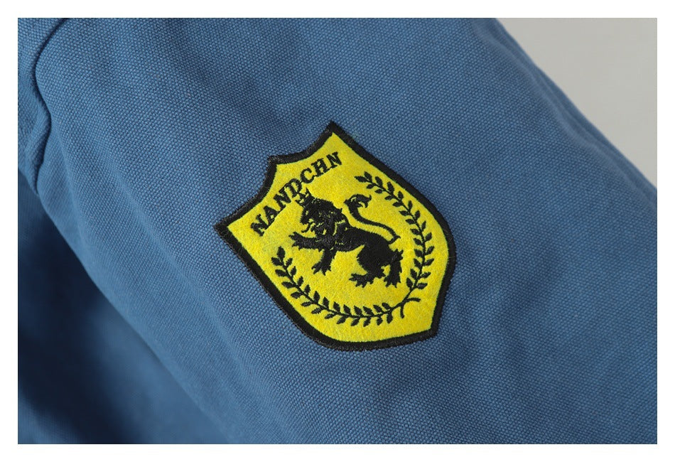 Close-up of blue textured fabric with a yellow embroidered shield patch featuring a black lion and lettering.