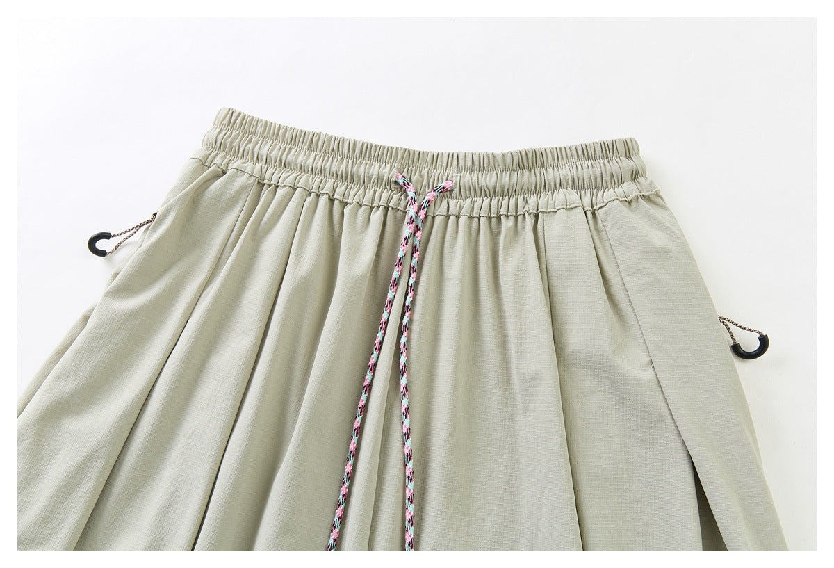 Close-up of pale sage pants showing the elastic waistband, pink patterned drawstring, and side cord toggles.