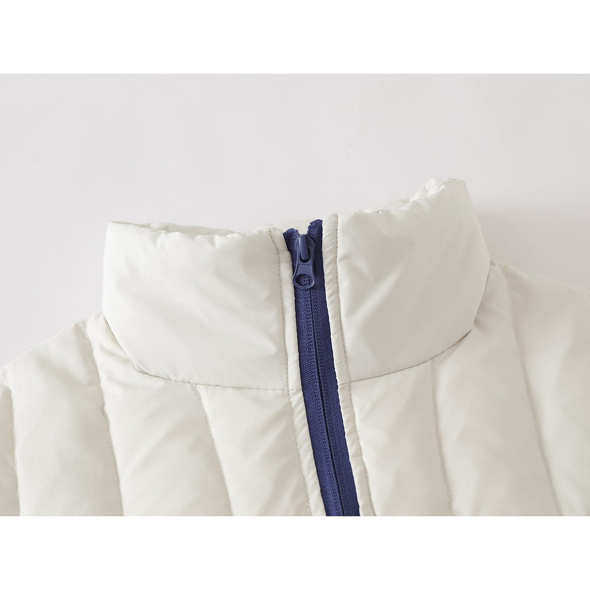 Close-up of an ivory quilted jacket's tall collar and dark blue front zipper.