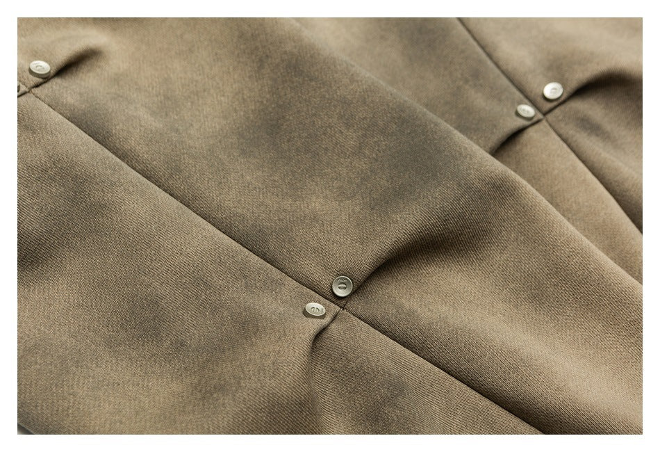 Close-up of taupe-brown garment fabric with diagonal seams and small pale buttons.