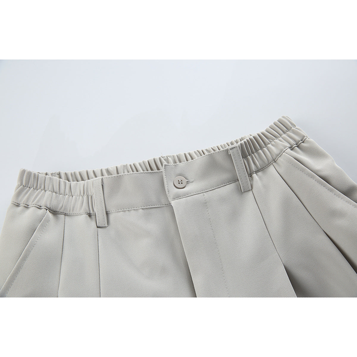 Close-up of light gray trousers showing the elasticated waistband, button closure, belt loops and front pleats.
