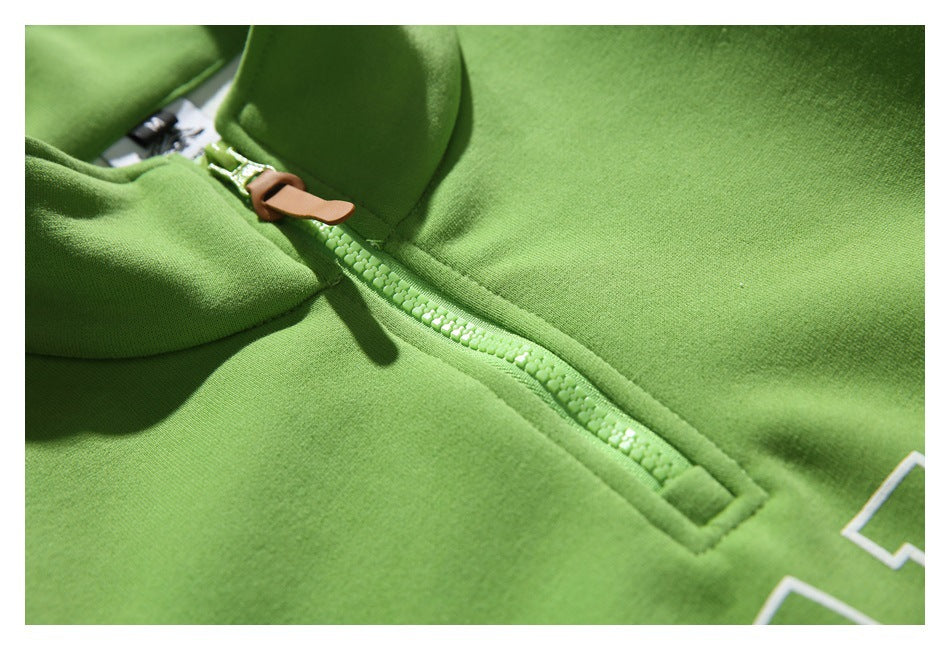 Close-up of the green pullover's quarter-zip track and stitched placket, with part of the chest lettering at the edge.