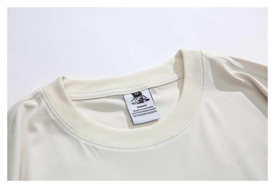 Close-up of the ivory T-shirt's ribbed crew neckline, shoulder stitching, and inside neck label.