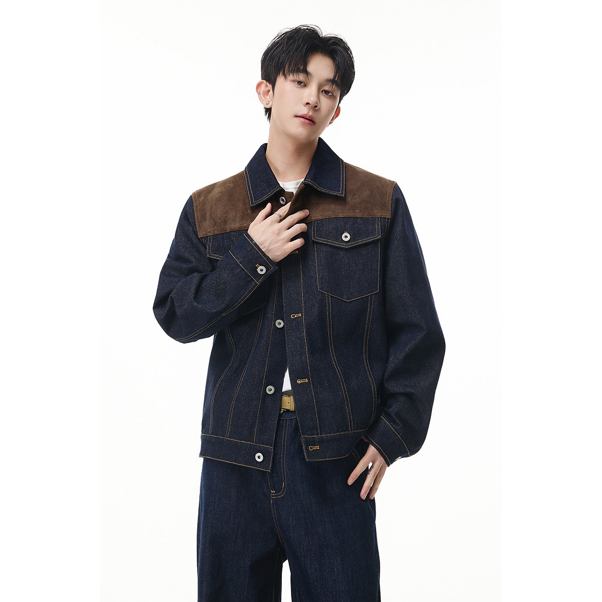Model wearing a dark indigo denim jacket with brown shoulder panels, contrast stitching and a chest pocket.