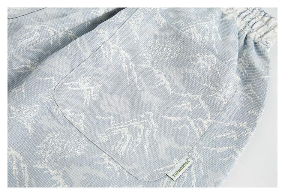 Close-up of a patch pocket and elastic waistband on pale blue mountain-print shorts.