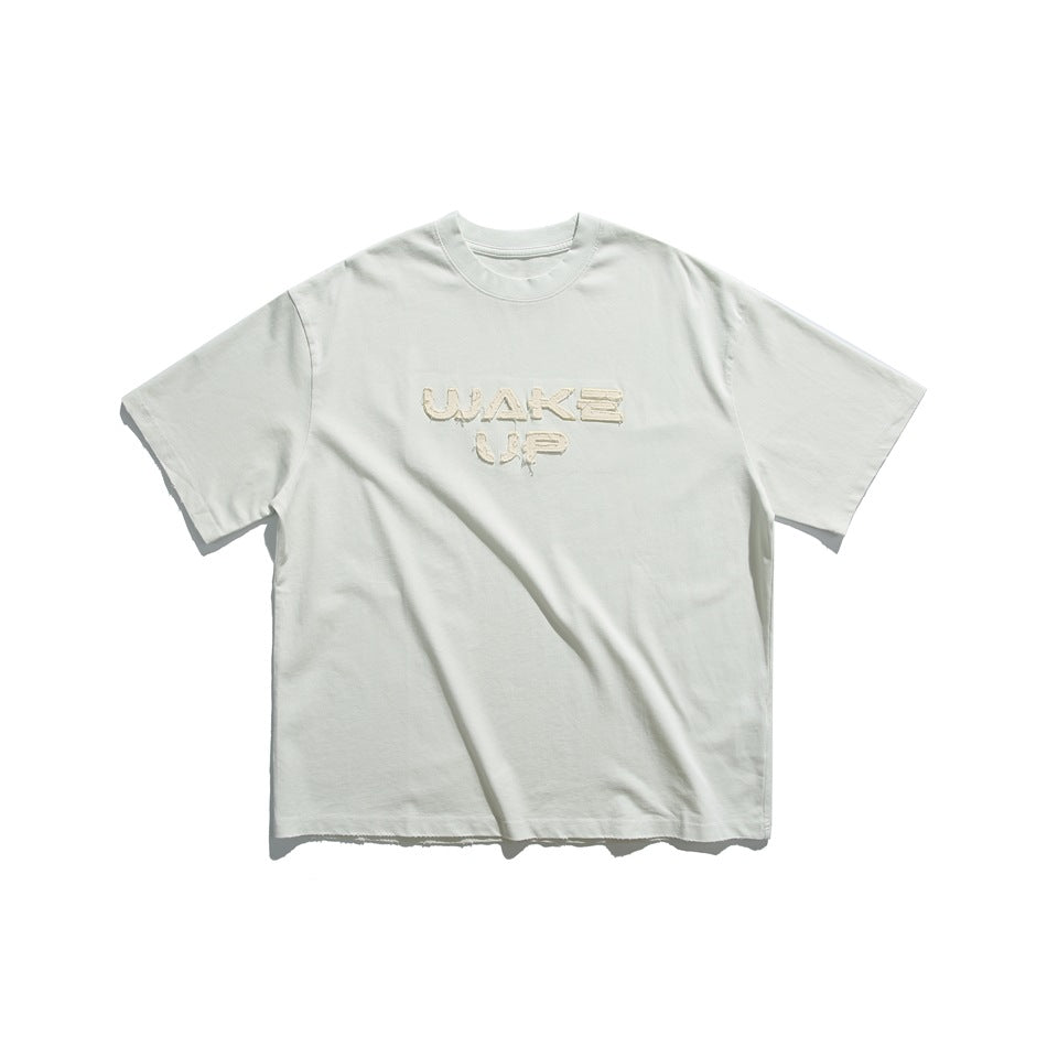 Pale light-blue short-sleeve T-shirt with frayed beige WAKE UP appliqué lettering on the chest, flat lay