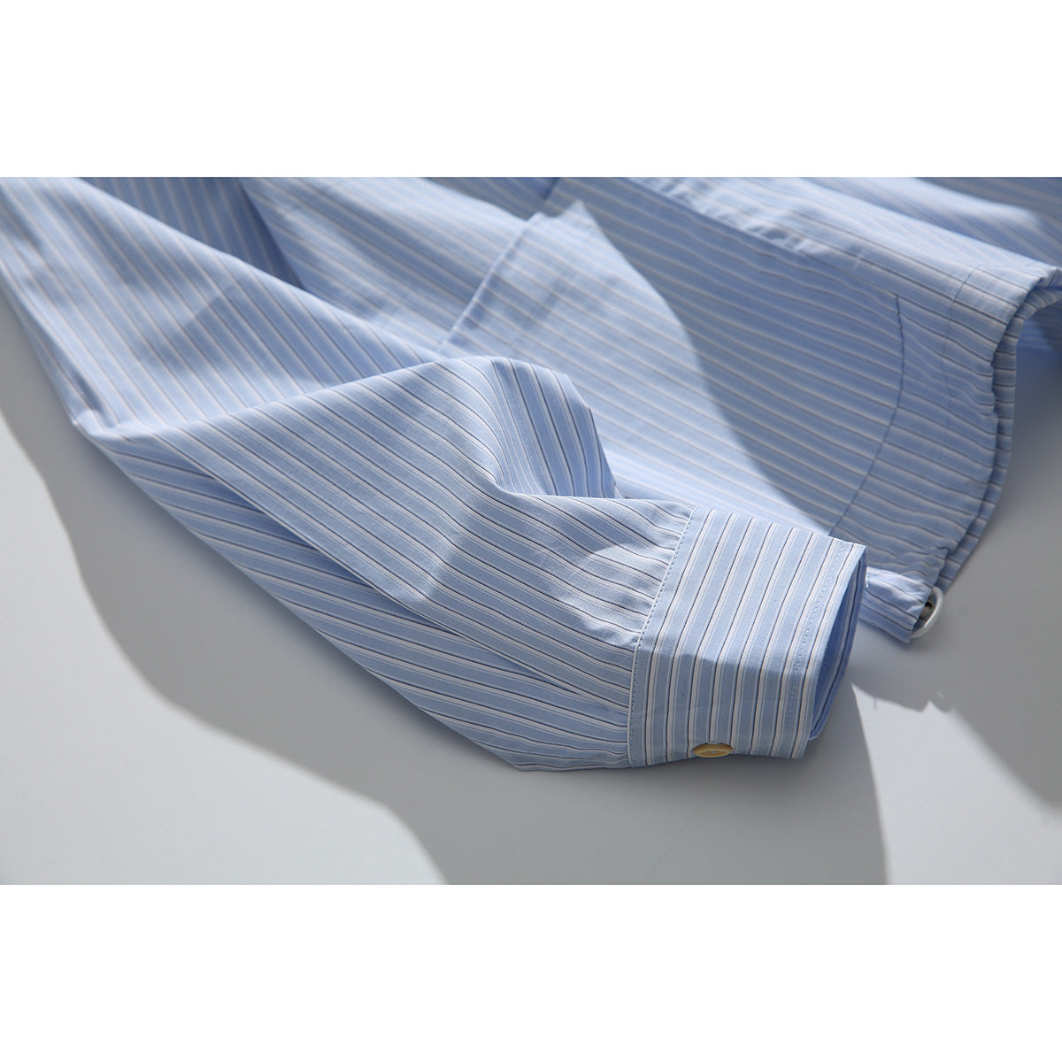 Detail of a light blue pinstriped sleeve and cuff with a button, against a pale background.
