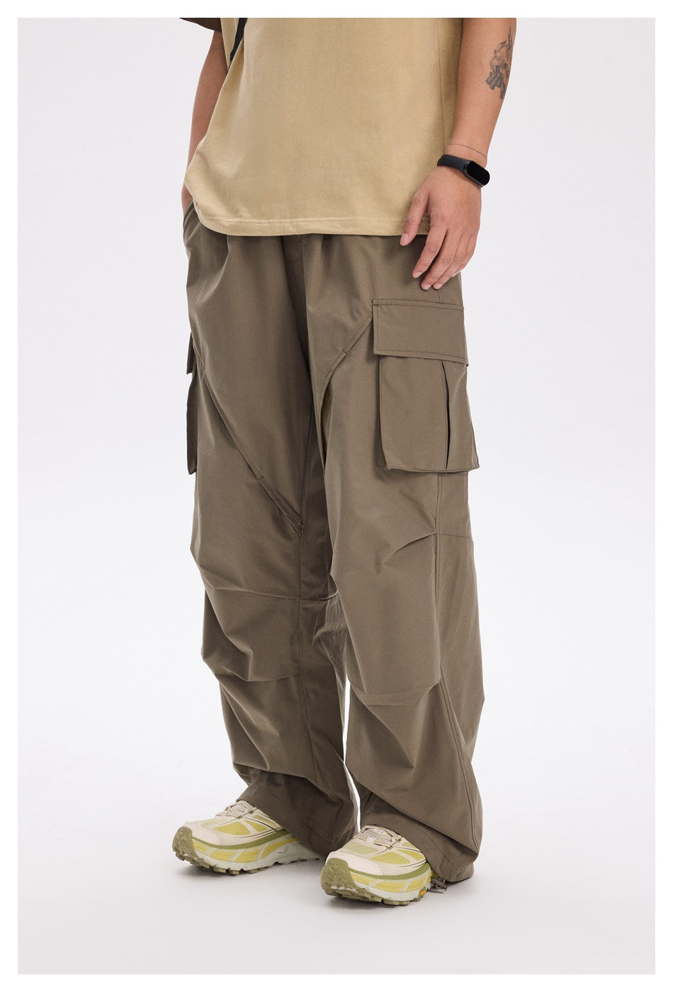 Person wearing army green wide-leg cargo pants with a flap pocket, tan T-shirt and light sneakers, front view