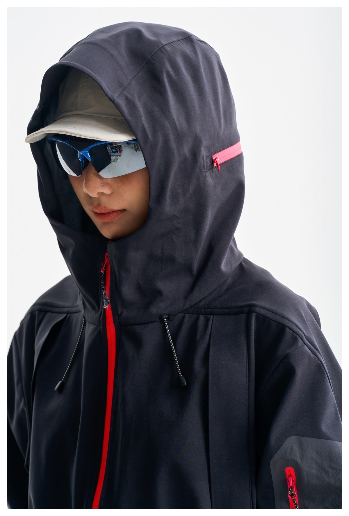 Close-up of a model wearing a dark hooded jacket with bright pink zippers and an adjustable hood.
