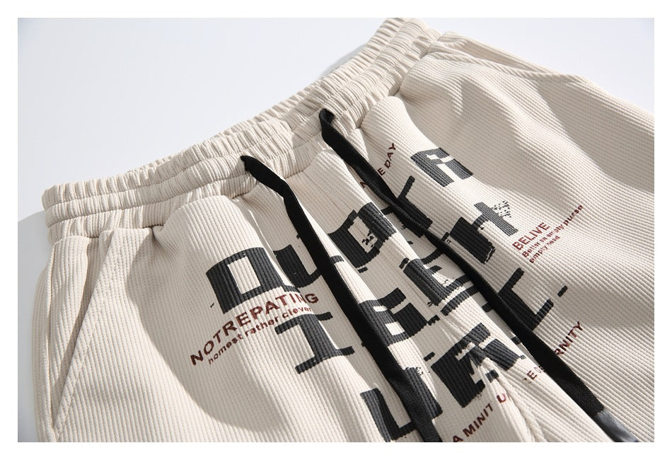 Close-up of ivory ribbed shorts with black drawstrings and bold black and brown printed lettering.