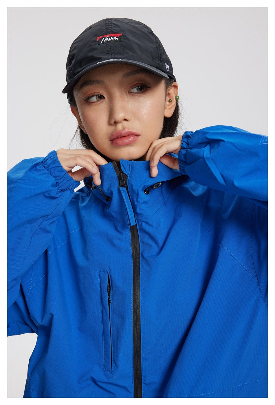 Close front view of a woman in a bright blue hooded jacket with a black center zipper and adjustable collar.