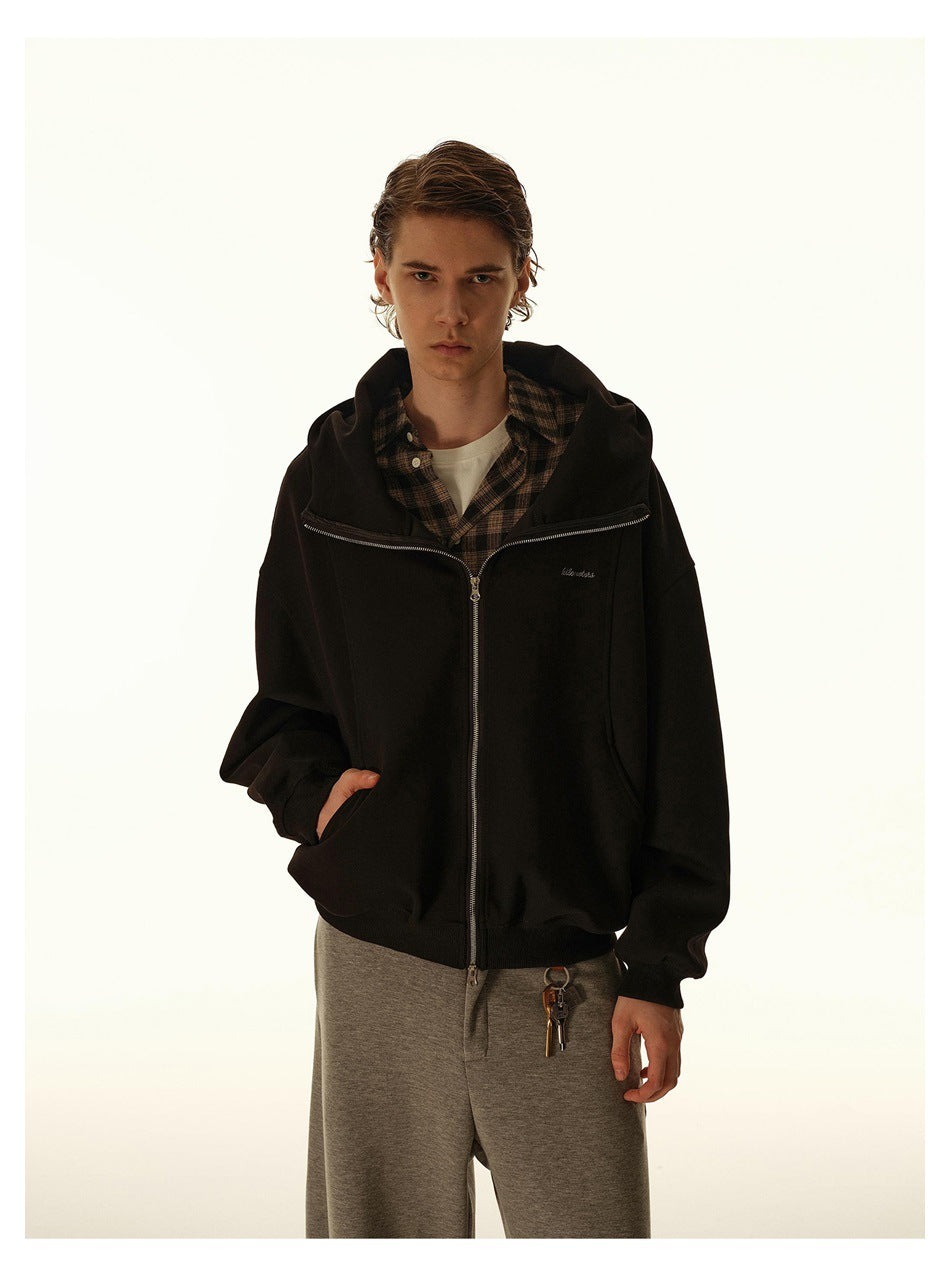 Closer front view of a model wearing a black zip-up hoodie over a brown plaid shirt.