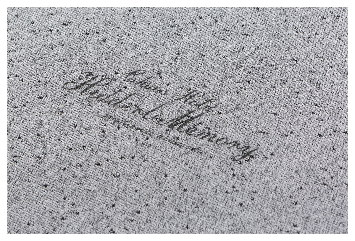 Close-up of light gray, dark-flecked knit fabric with a small cursive embroidered inscription.