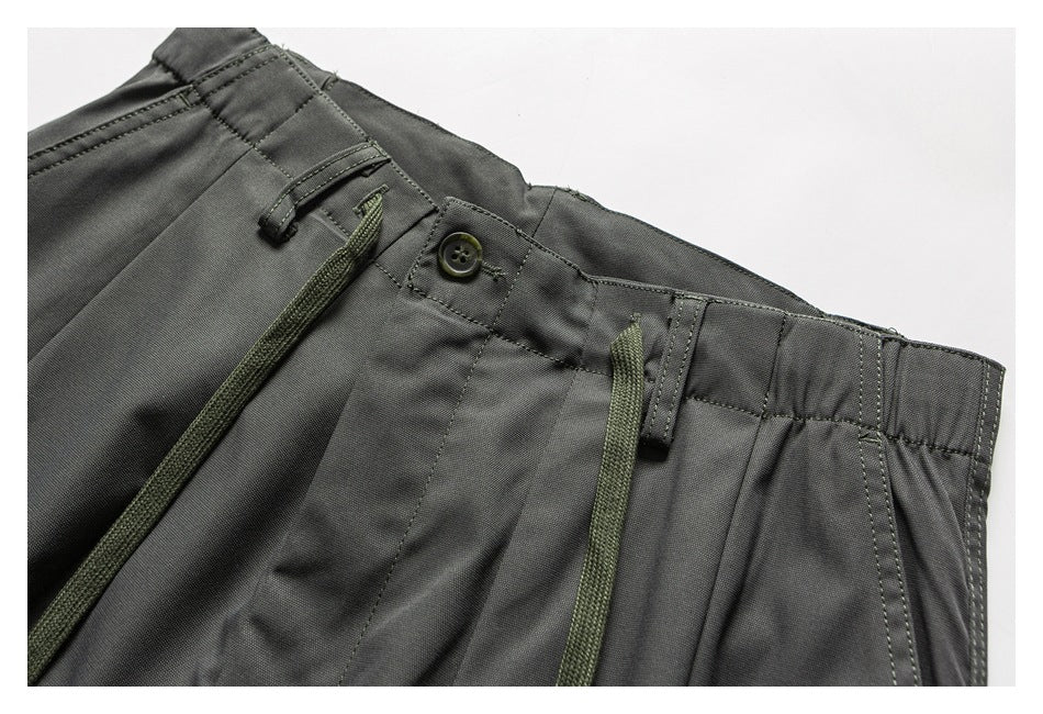 Close-up of charcoal trousers showing the front waistband, button, belt loops, and olive drawstring.